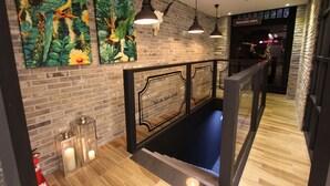 Un hall d’entrée avec un mur en briques, un plancher en bois et des œuvres d’art représentant des oiseaux et du feuillage. On y trouve des suspensions lumineuses et un panneau indiquant l’emplacement du service de dépôt de bagages.