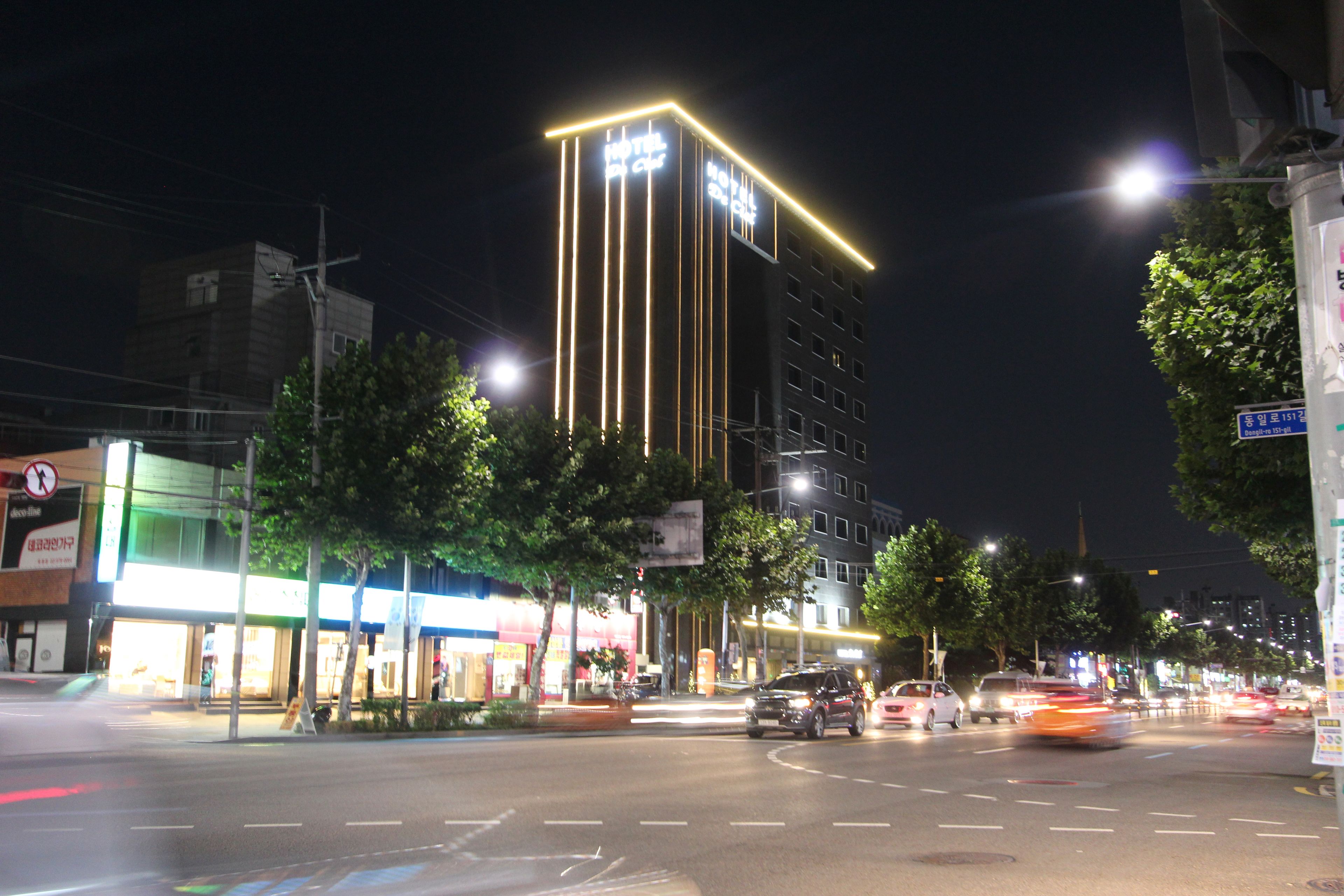 A multi-story hotel with illuminated vertical lines on the facade, a well-lit street with cars, and a clear night sky.