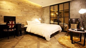 Une chambre moderne avec un mur en bois, un grand lit, un bureau avec une chaise et une table ronde avec une lampe.