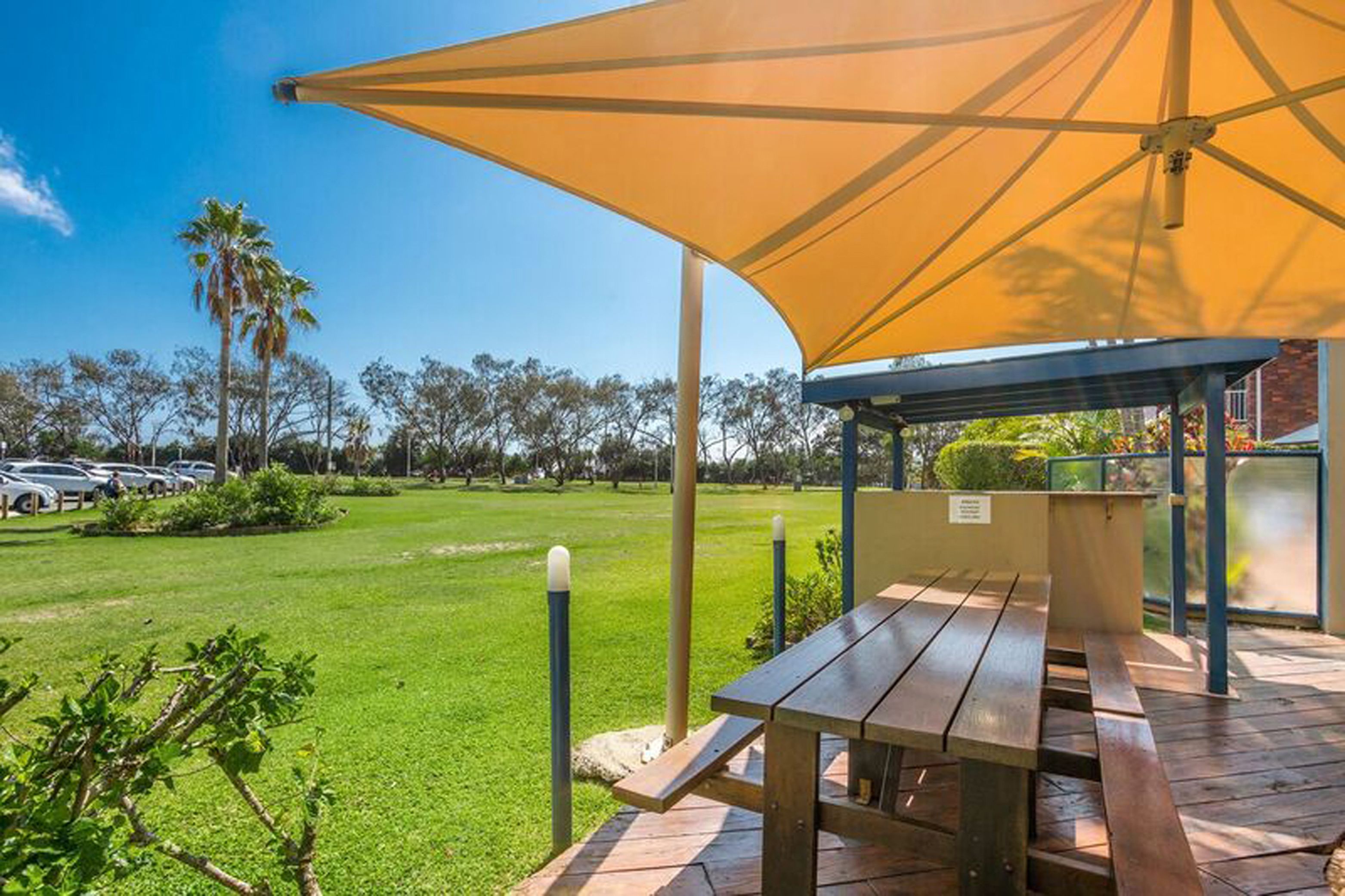 A covered picnic area with a table and benches, surrounded by a grassy lawn and trees.