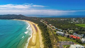 An aerial view of a coastal area with a beach, residential buildings, and a road. - Byron Bay Beachfront Apartments (Byron Bay)