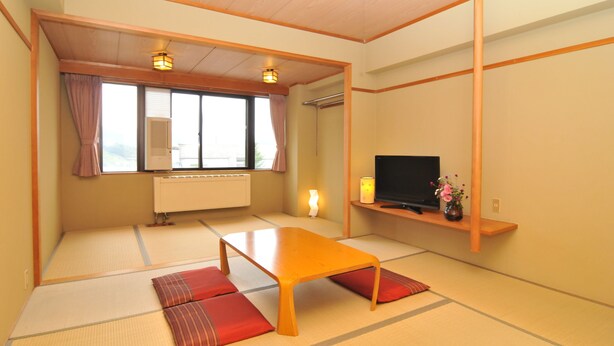 A traditional Japanese room with tatami flooring, a low wooden table, a television on a shelf, and a window with curtains.