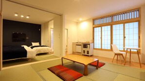 A room with two beds, a small kitchenette, a tatami mat, and a large window.