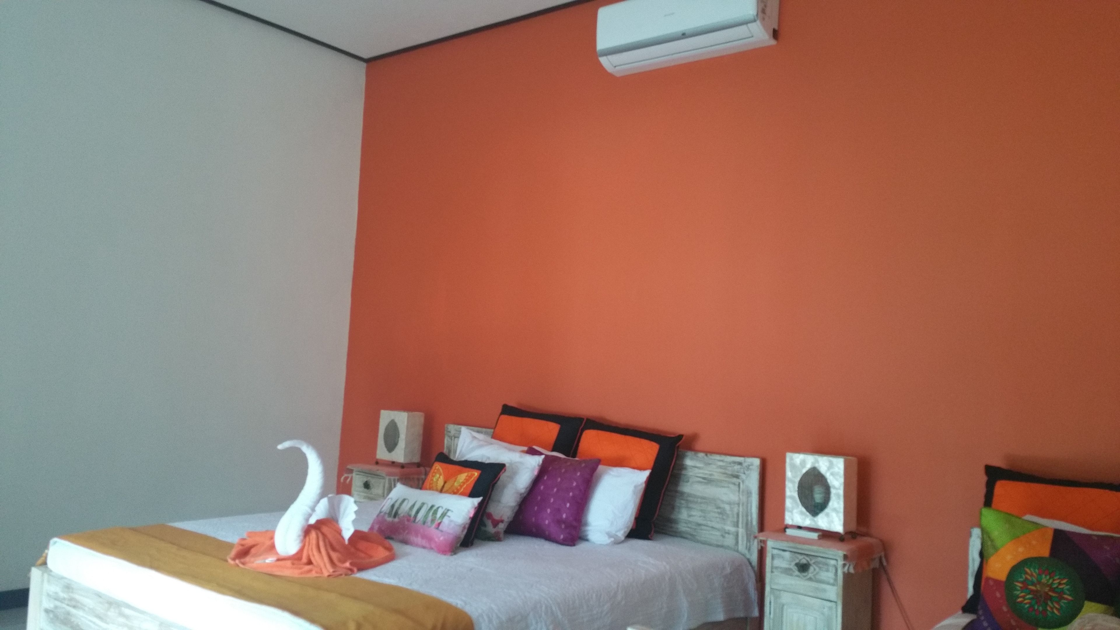 A bedroom with a bed, pillows, a decorative swan, a white air conditioner, and a nightstand with a speaker.
