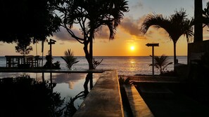 A serene sunset view over a reflective pool with palm trees and a signpost. - Nalini Resort (Karangasem)
