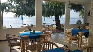 A restaurant with outdoor seating overlooking the sea, featuring wooden tables and chairs, and a view of the ocean through large windows. - Nalini Resort (Karangasem)