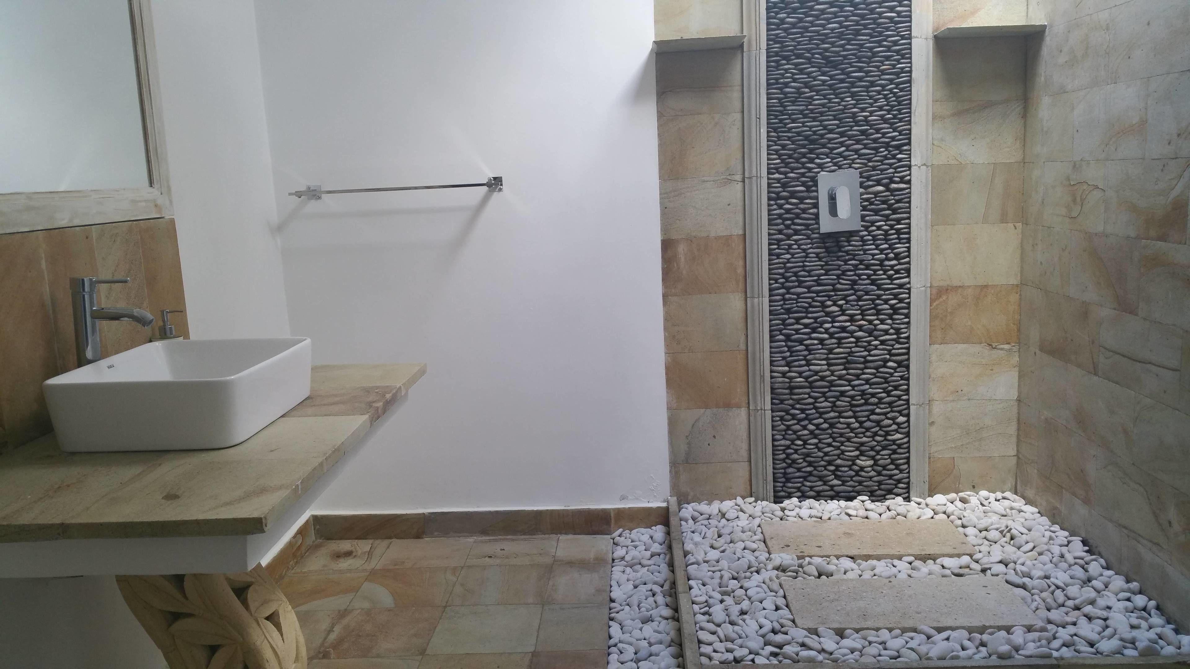 A bathroom with a white sink, a wooden vanity, a towel rack, and a shower area with stone walls and pebbles.