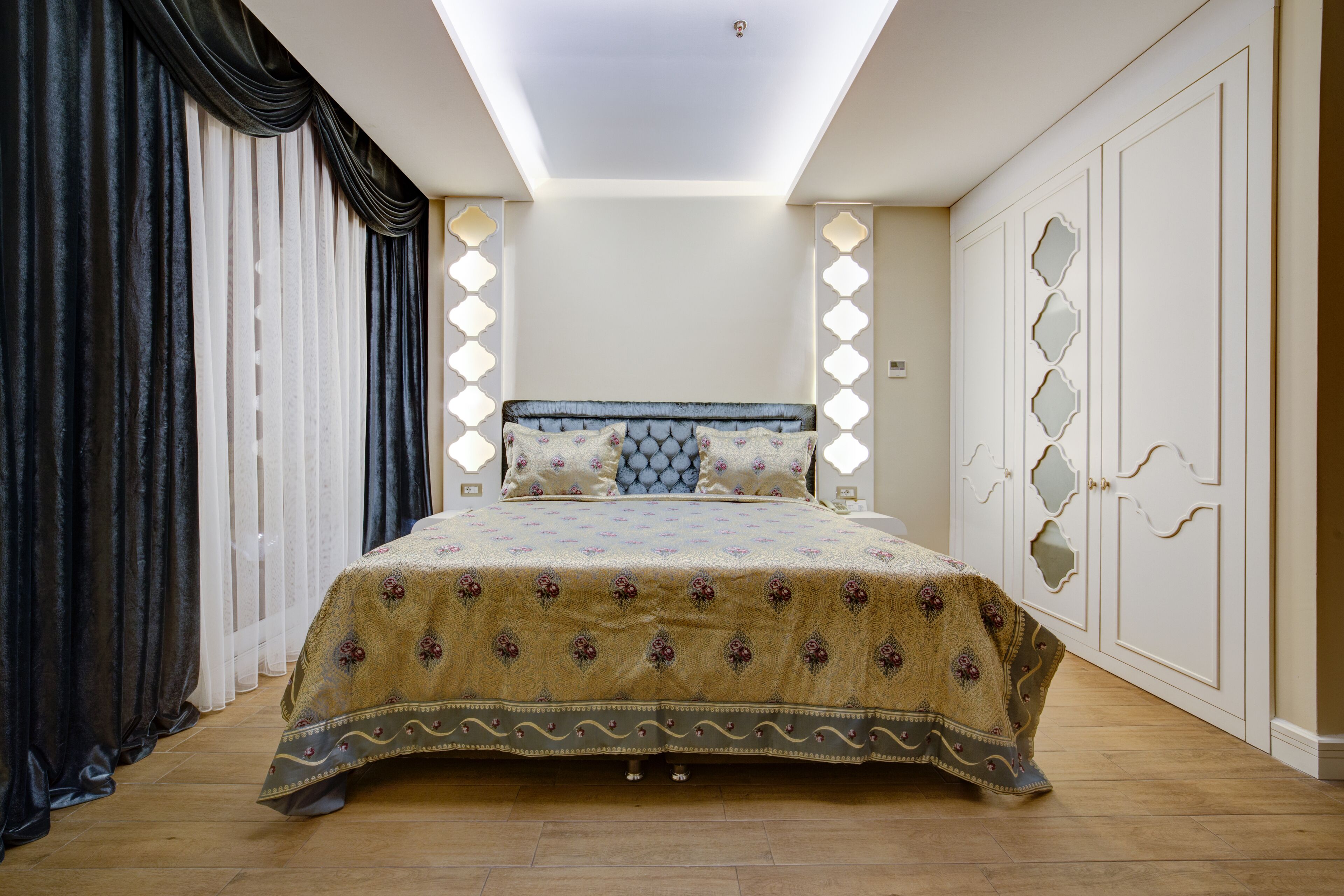 A bedroom with a large bed, a ceiling light, a wardrobe, and a window with curtains.