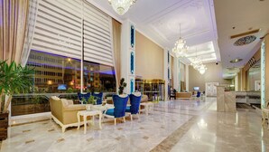 Een ruime lobby met een hoge plafond, kroonluchters en een zithoek met sofa's en fauteuils.