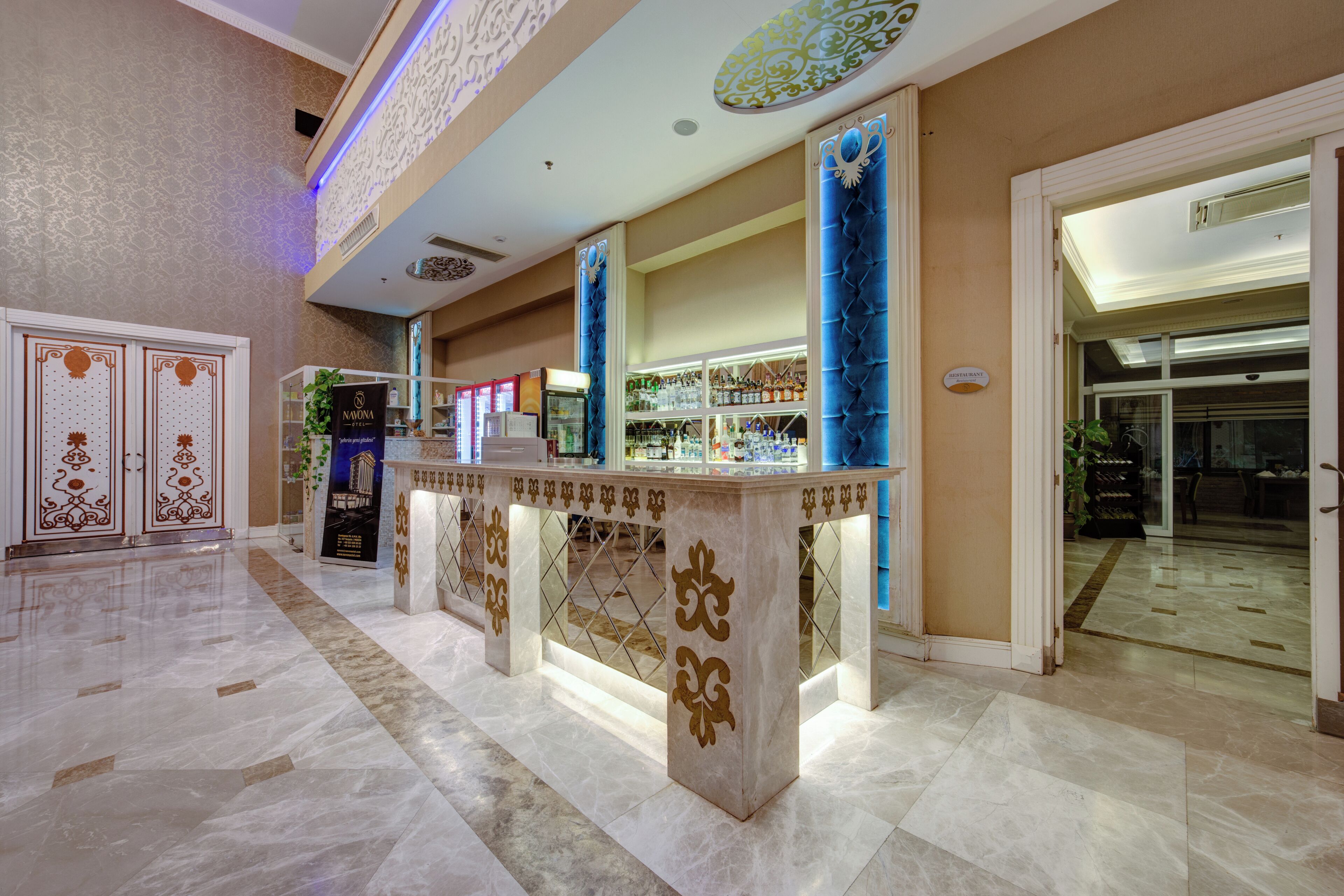 A hotel lobby with marble flooring, a reception desk, and a glass door leading to a dining area.