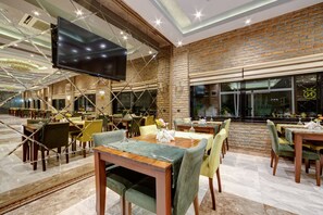 Un restaurant spacieux, doté de nombreuses tables et chaises, d’un grand téléviseur à écran plat fixé au plafond et d’un mur en briques agrémenté de grandes fenêtres.