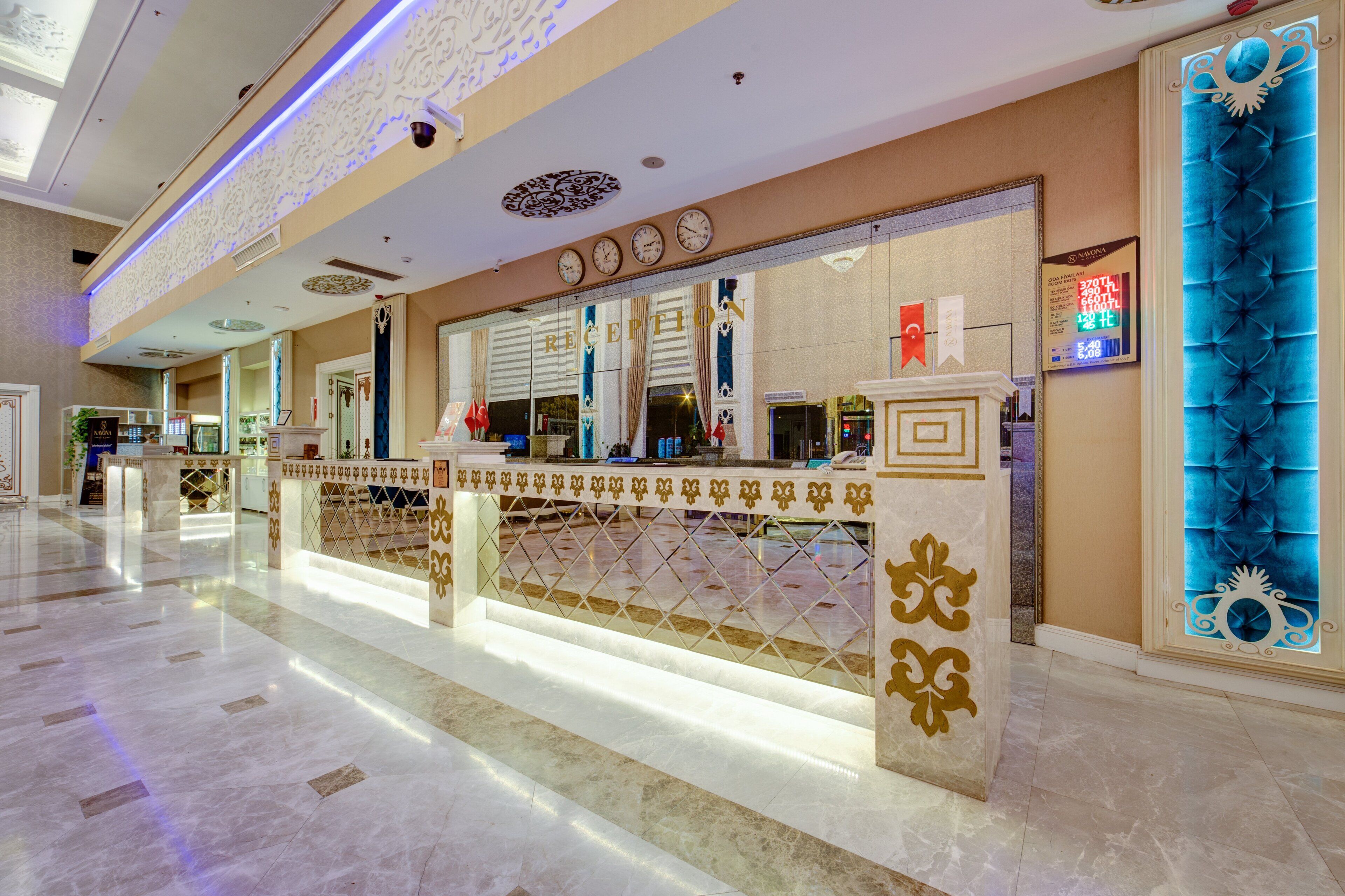 Zona de recepción de hotel con suelo de mármol, mostrador de recepción con separador decorativo y un elemento mural iluminado en azul.