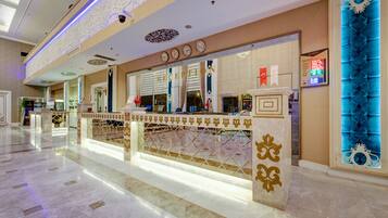 Zona de recepción de hotel con suelo de mármol, mostrador de recepción con separador decorativo y un elemento mural iluminado en azul.