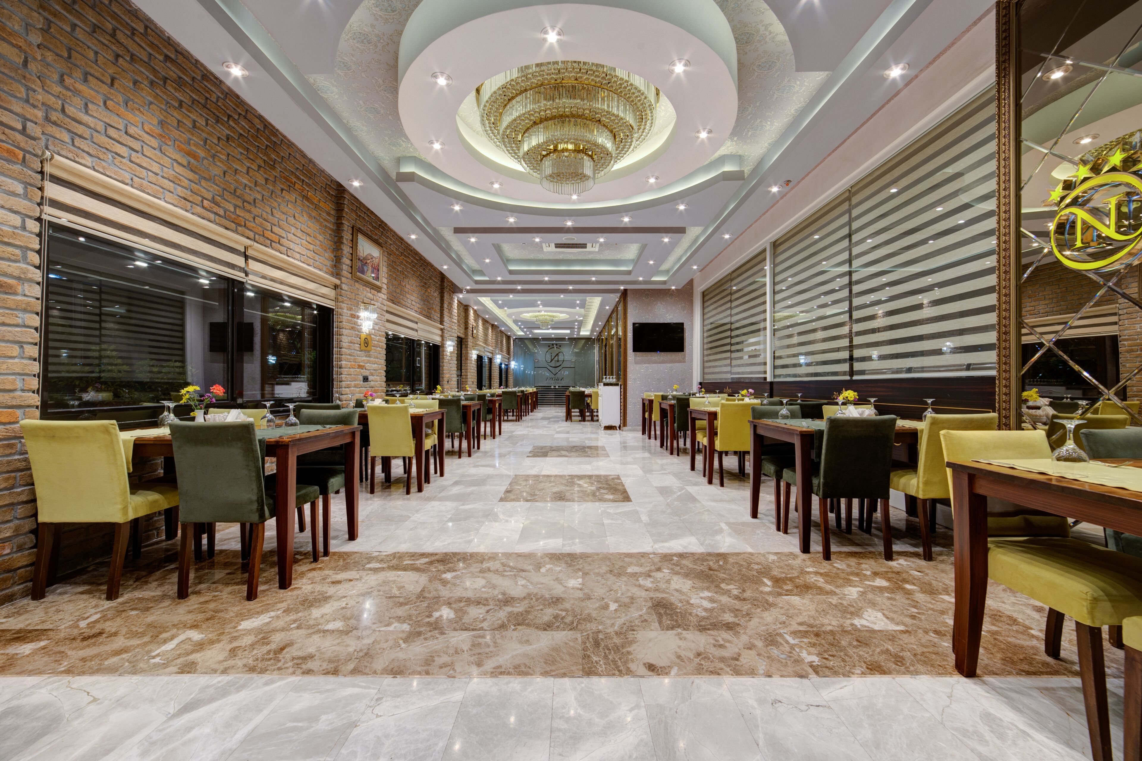 A spacious hotel lobby with a long reception desk, multiple seating areas, and a chandelier.