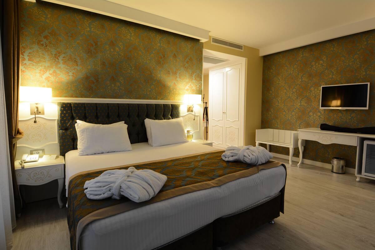 A hotel room with a large bed, two bedside tables with lamps, a desk, and a television on the wall.