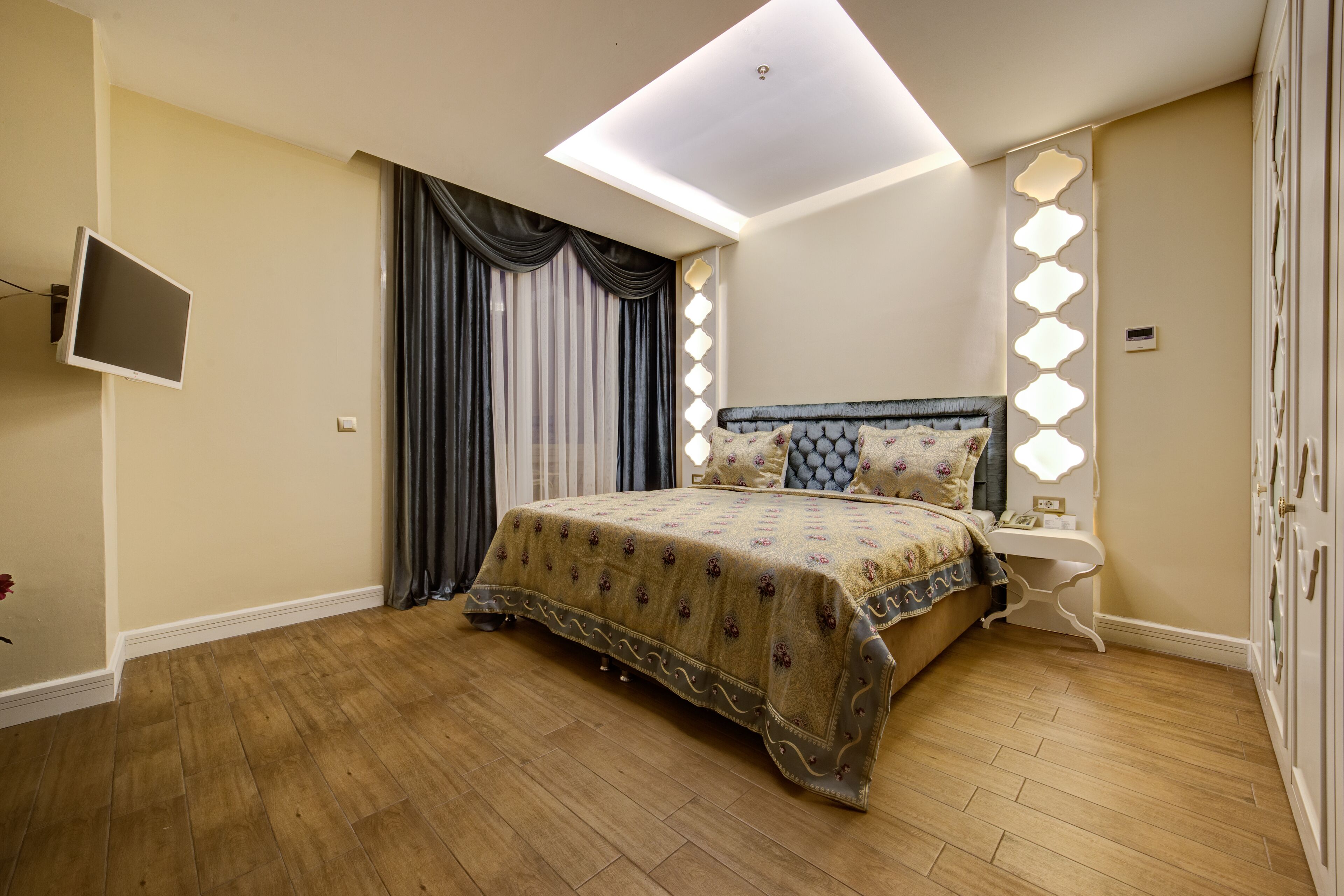 A bedroom with a bed, a nightstand, a TV mounted on the wall, and a skylight.