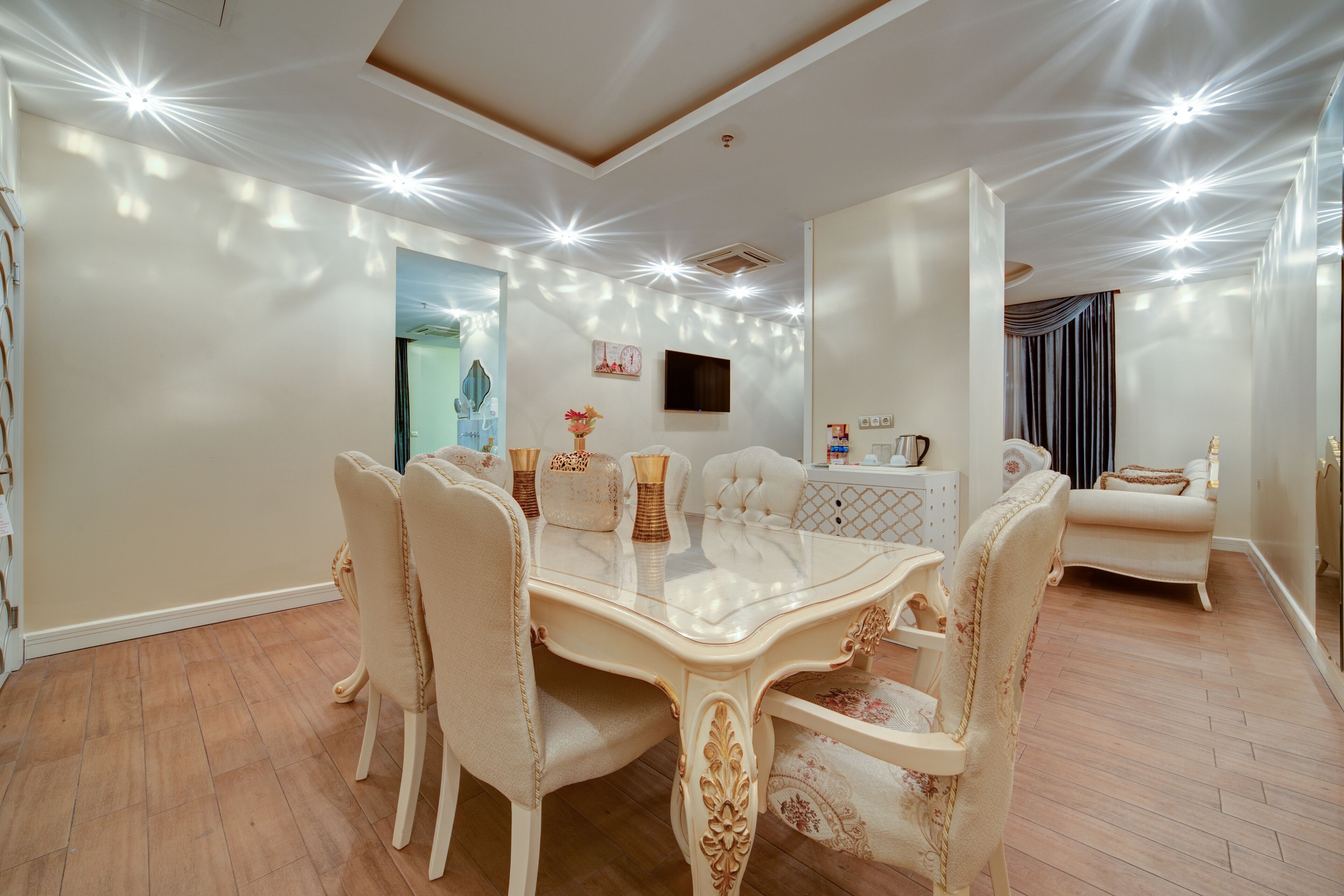 A dining area with a large table and chairs, a flat-screen TV mounted on the wall, and a sofa in the background.