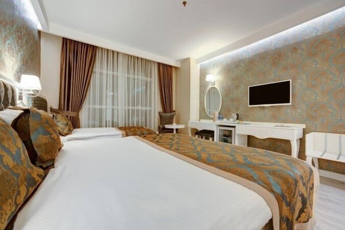 A hotel room with a large bed, a desk with a mirror, a television, and a window with curtains.