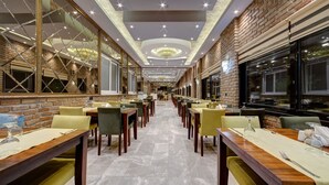 Een ruim restaurant met lange tafels en stoelen, een bakstenen muur en een kroonluchter.