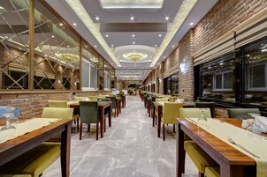 Um restaurante espaçoso com mesas e cadeiras compridas, uma parede de tijolos e um lustre.