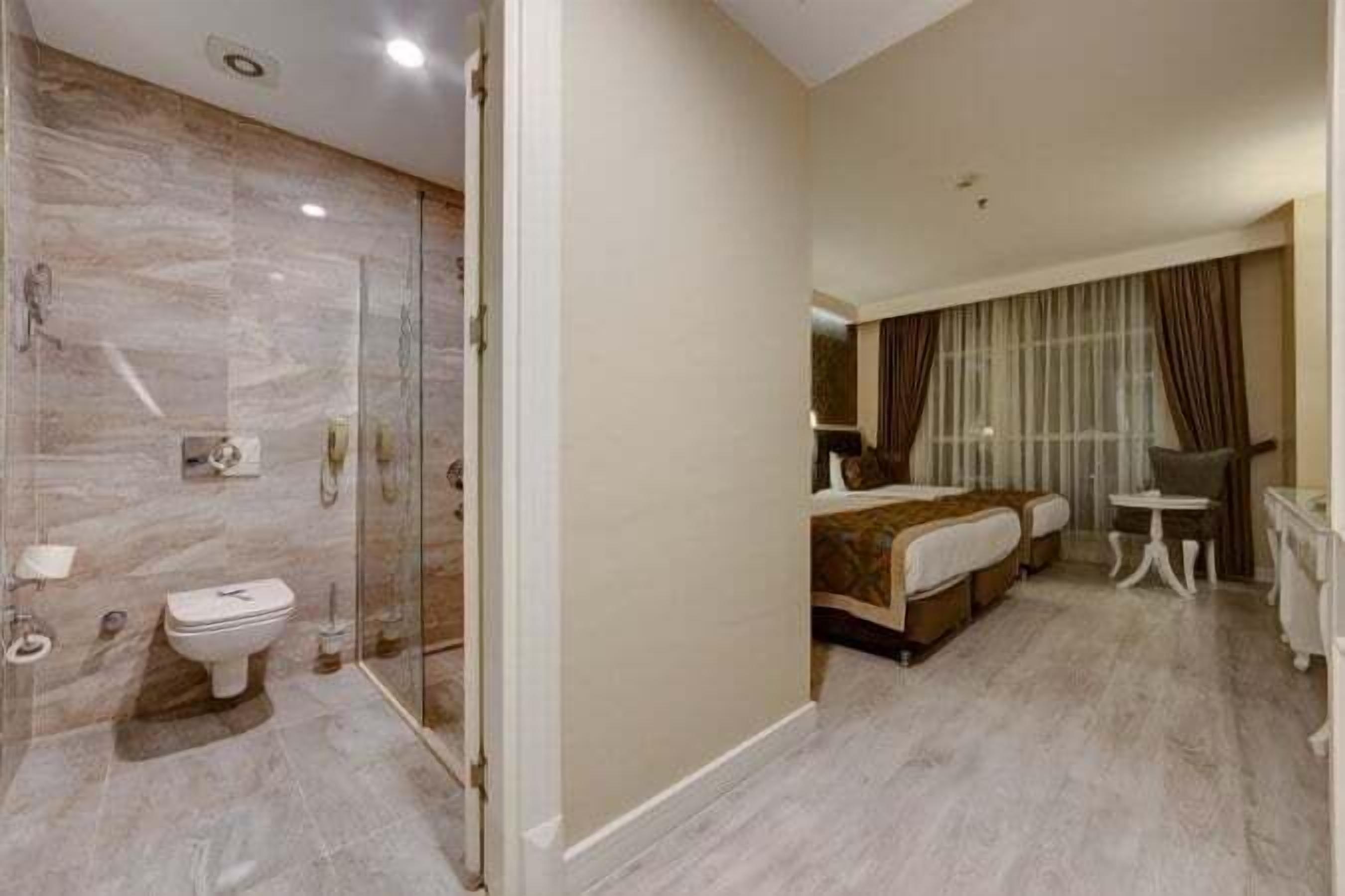 Una habitación de hotel con baño, cama, mesita de noche y espejo.