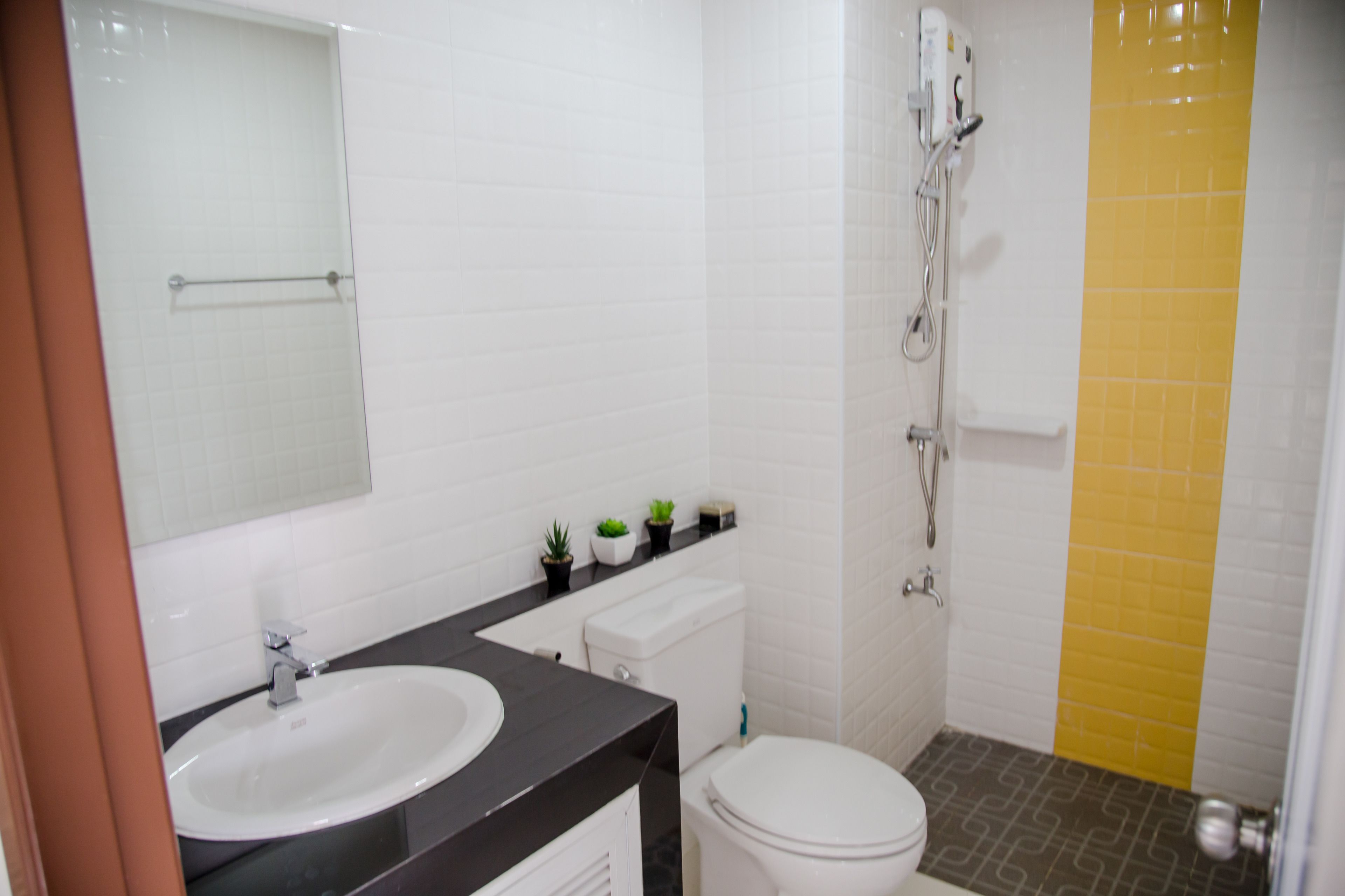 A bathroom with a white sink, toilet, and shower. There are small plants on the countertop.