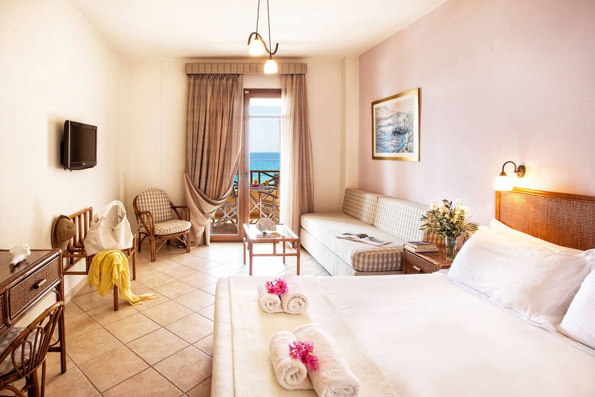 Habitación de hotel con cama, sofá, escritorio, silla, televisor y vista al mar.