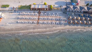 An aerial view of a beach resort with rows of sun loungers, a wooden deck, and a building with a sloped roof.