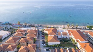 Vue aérienne d’une ville côtière avec des bâtiments aux toits de tuiles rouges, une plage et un port de plaisance.