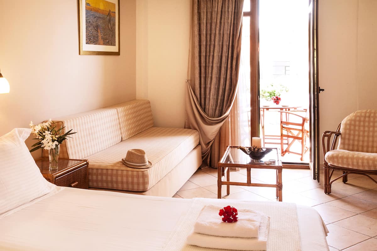 Habitación de hotel con cama, sofá, una mesita con vela, una silla y vistas al exterior.