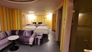 Une chambre d’hôtel avec un canapé violet, une petite table ronde et deux lits.