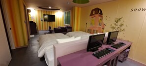 A hotel room with two beds, a desk with computers, a TV, and a mural on the wall.