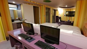 Une chambre d’hôtel avec deux lits, un bureau équipé de deux ordinateurs, une télévision et une salle de bain avec un miroir et un lavabo.