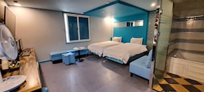 A bedroom with two beds, a desk with a chair, a fan, and a window.