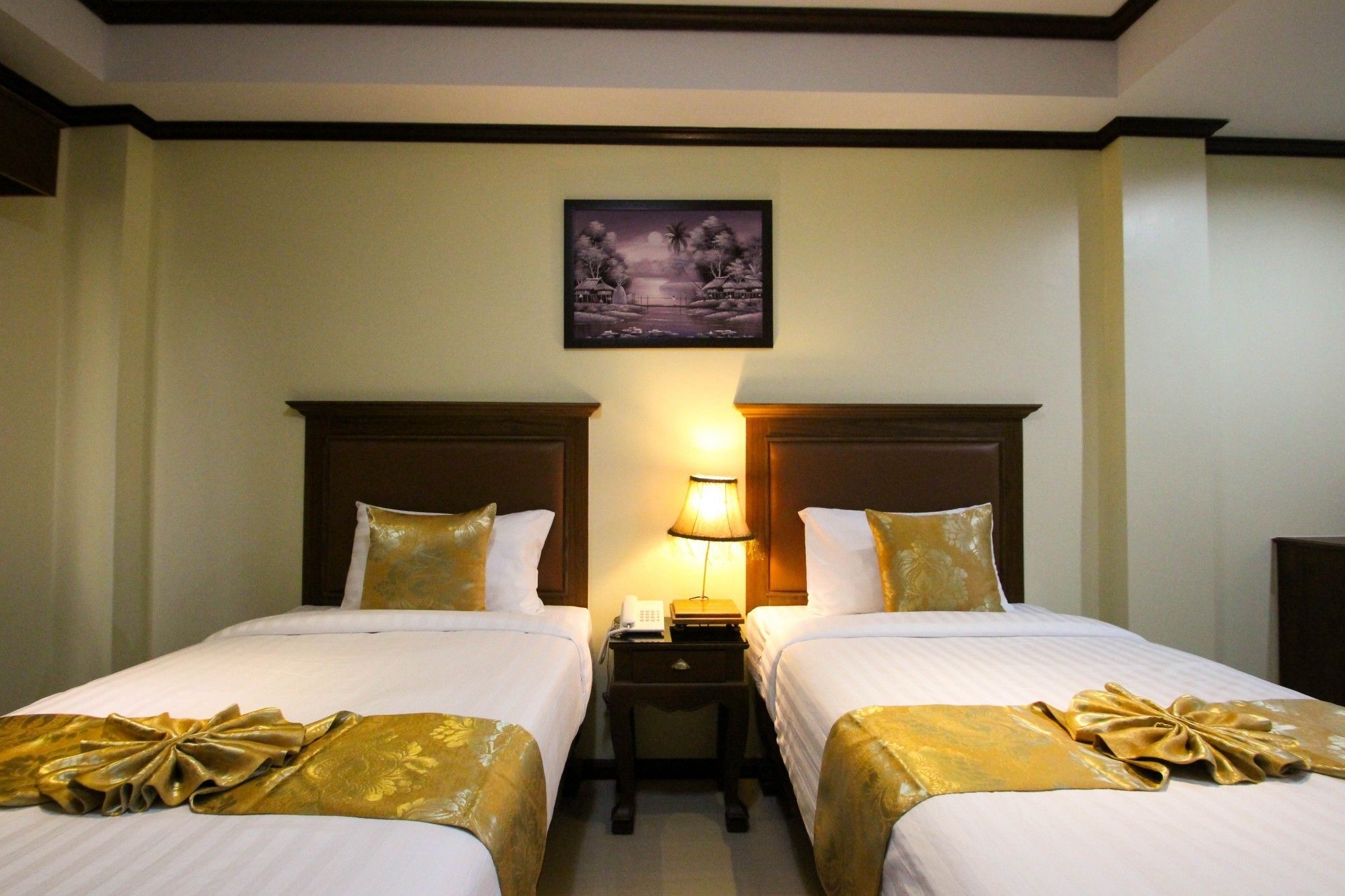 A hotel room with two beds, a nightstand with a lamp, and a framed picture on the wall.