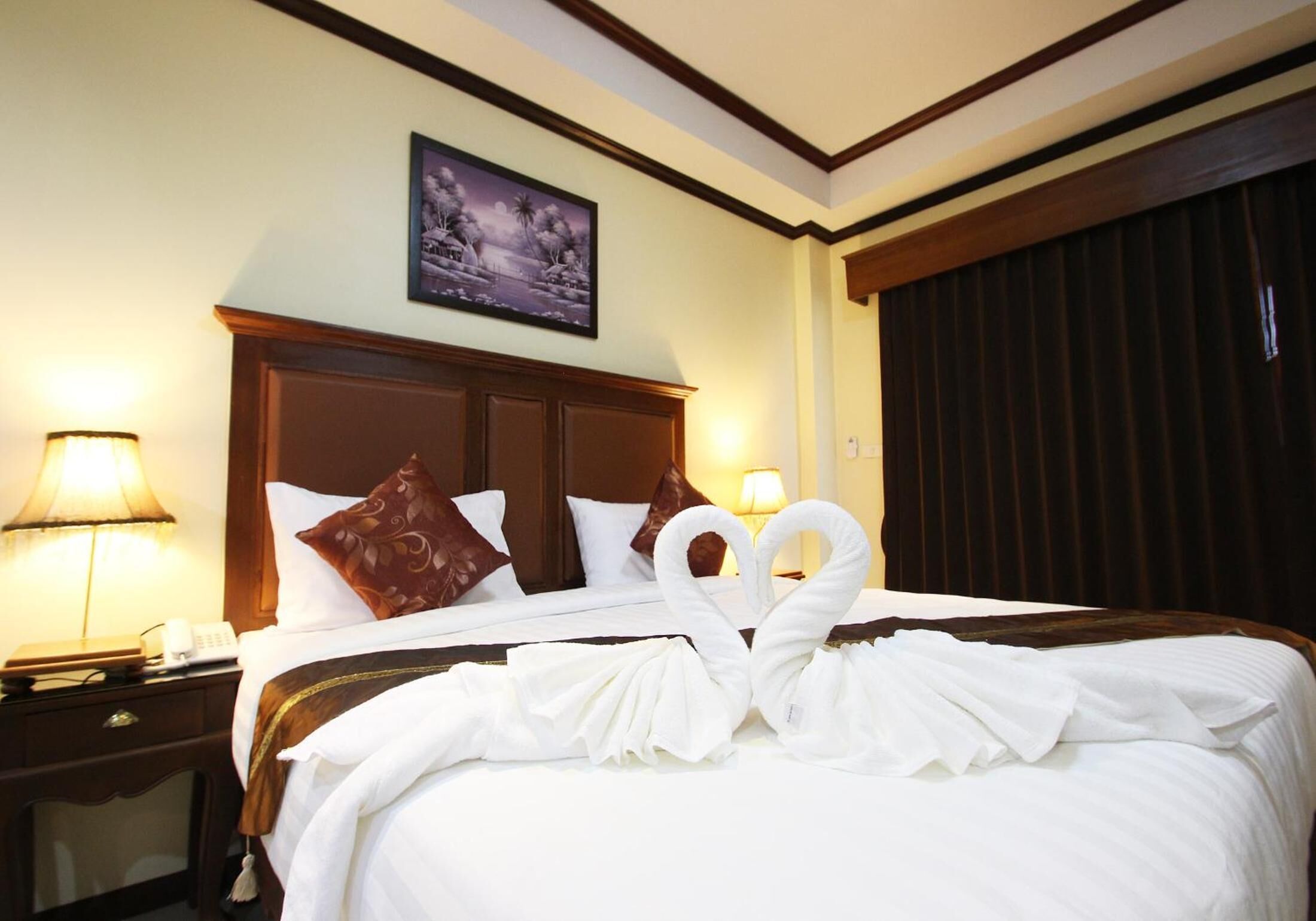 A hotel room with a neatly made bed, two lamps on either side, a wooden headboard, and a framed picture on the wall.