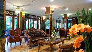 A lobby with a traditional wooden sofa, leather armchairs, a glass coffee table, and a decorative mirror. - I Boutique Hotel (Pluak Daeng)