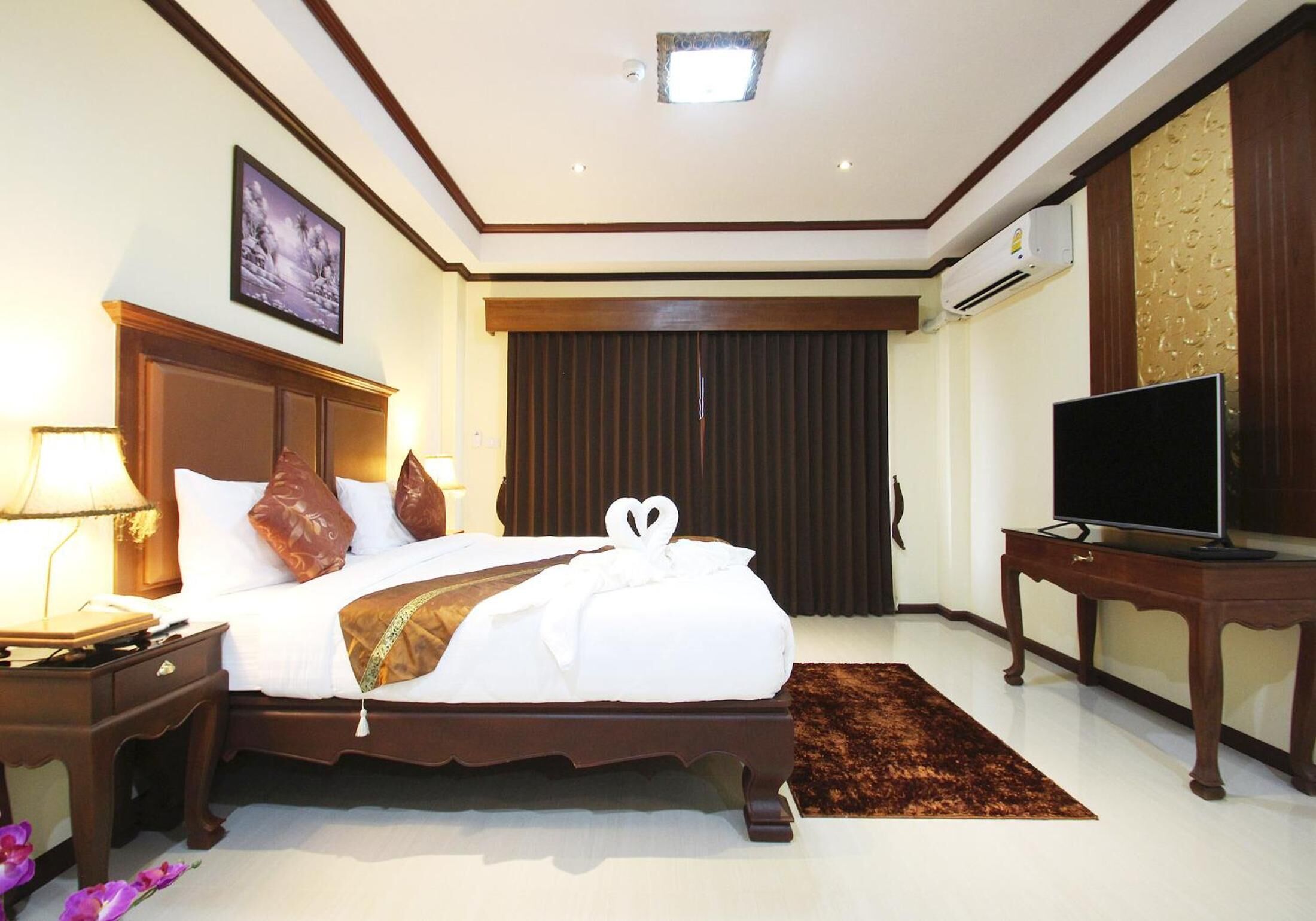 Una habitación de hotel con una cama grande, televisión, mesita de noche, lámpara y un cuadro en la pared.