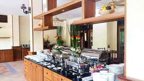 A buffet setup with various food stations, a wooden counter, and a decorative vase with flowers. - I Boutique Hotel (Pluak Daeng)