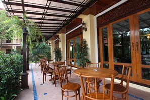 An outdoor patio area with wooden tables and chairs, surrounded by potted plants and large windows. - I Boutique Hotel (Pluak Daeng)