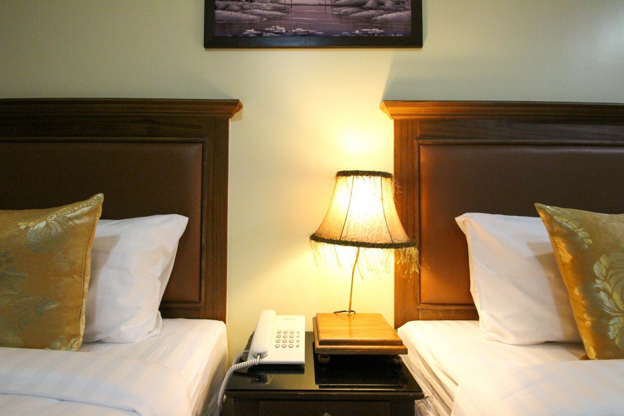 A hotel room with two beds, each with a wooden headboard, a bedside lamp, and a telephone.