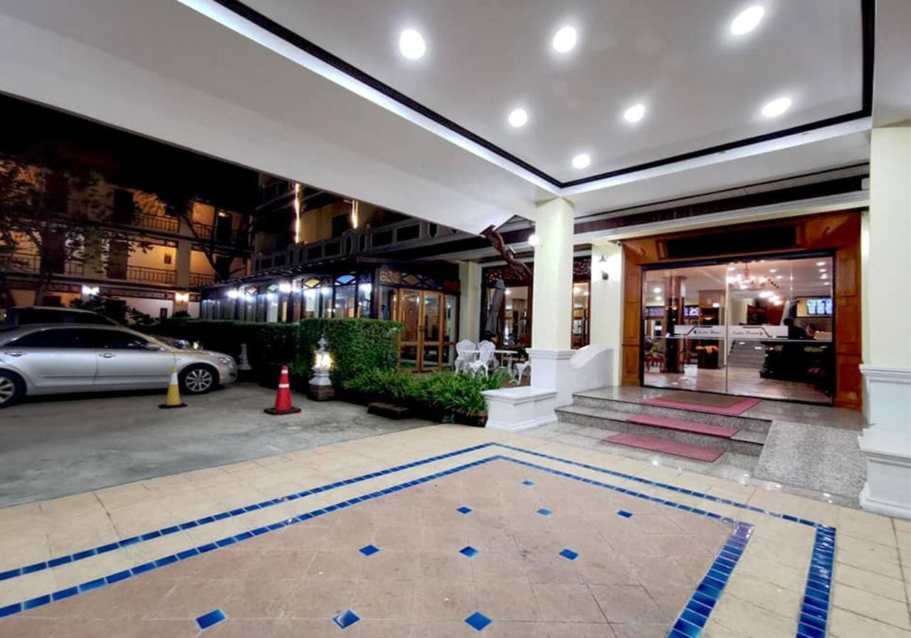 A hotel entrance with a tiled area, a car parked outside, and a building with glass doors.