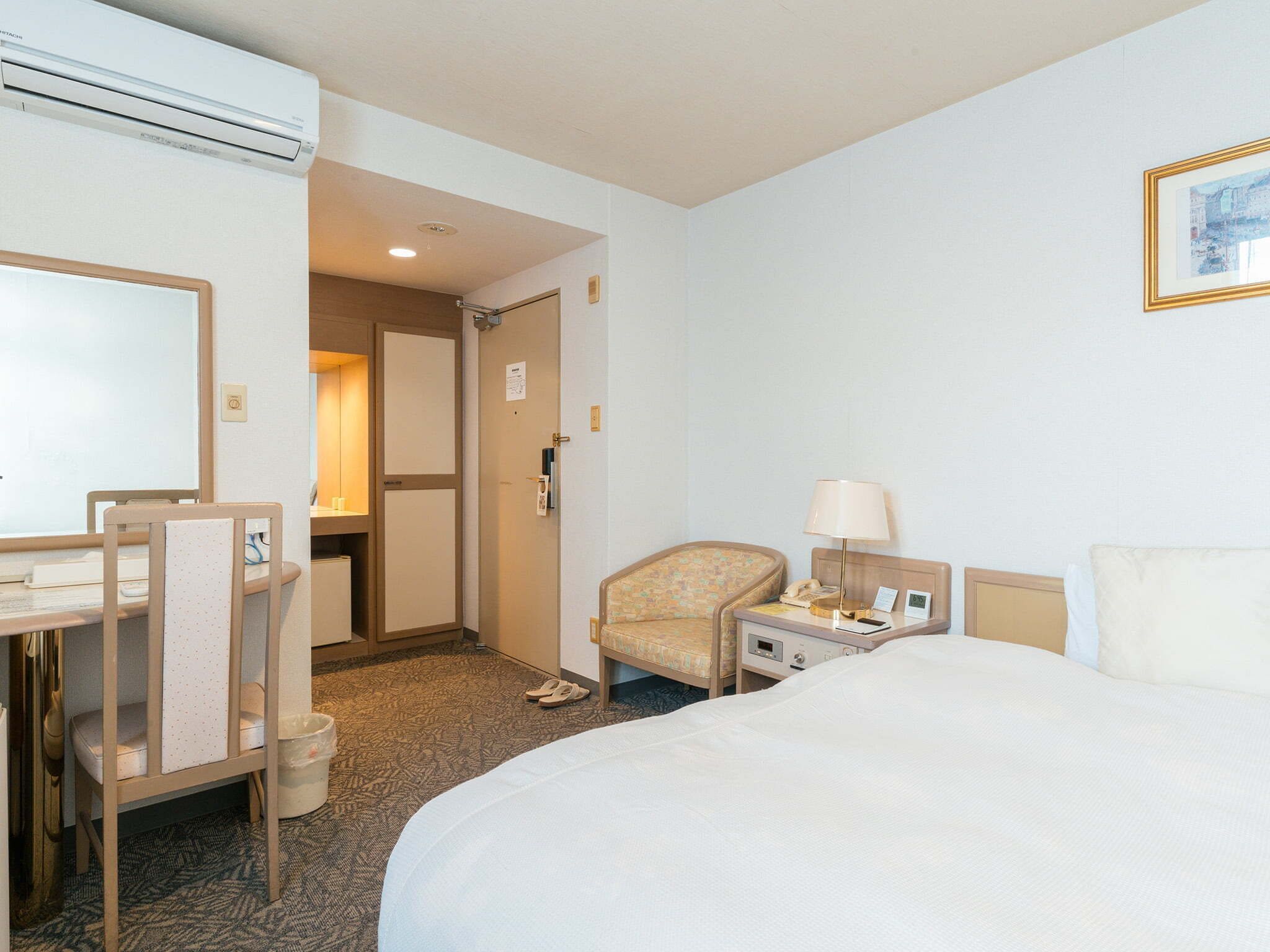 Una habitaci ón de hotel con cama, escritorio, silla, mesita de noche y puerta que da a un baño.