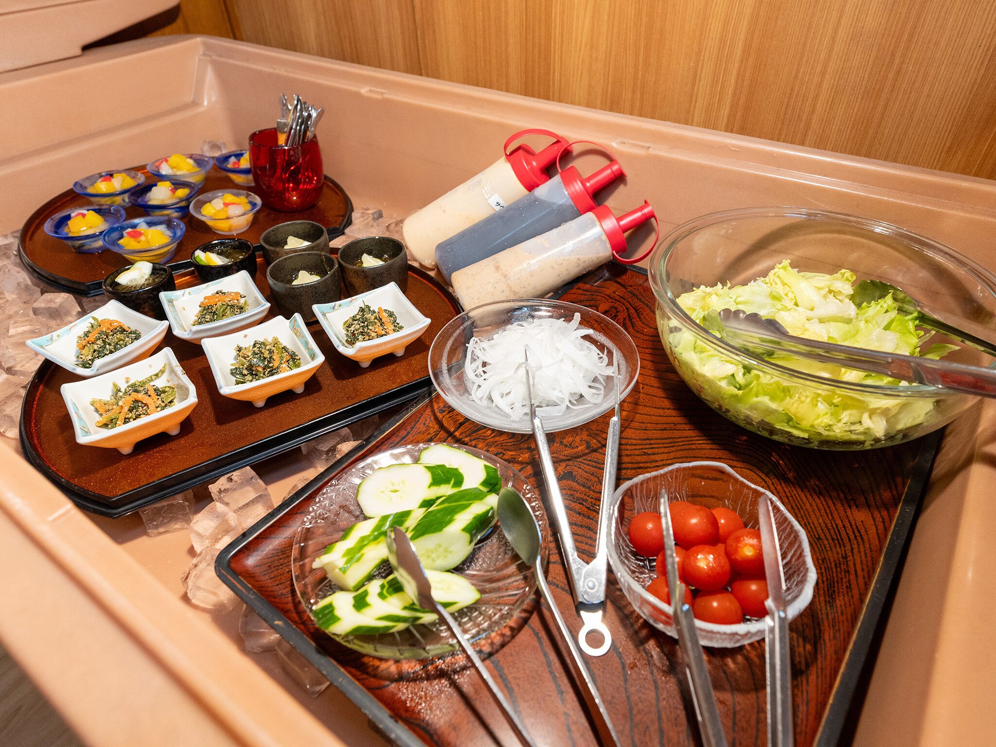 Een dienblad met diverse soorten eten, waaronder saladeschalen, plakjes komkommer, cherrytomaten en kleine schaaltjes met verschillende toppings.