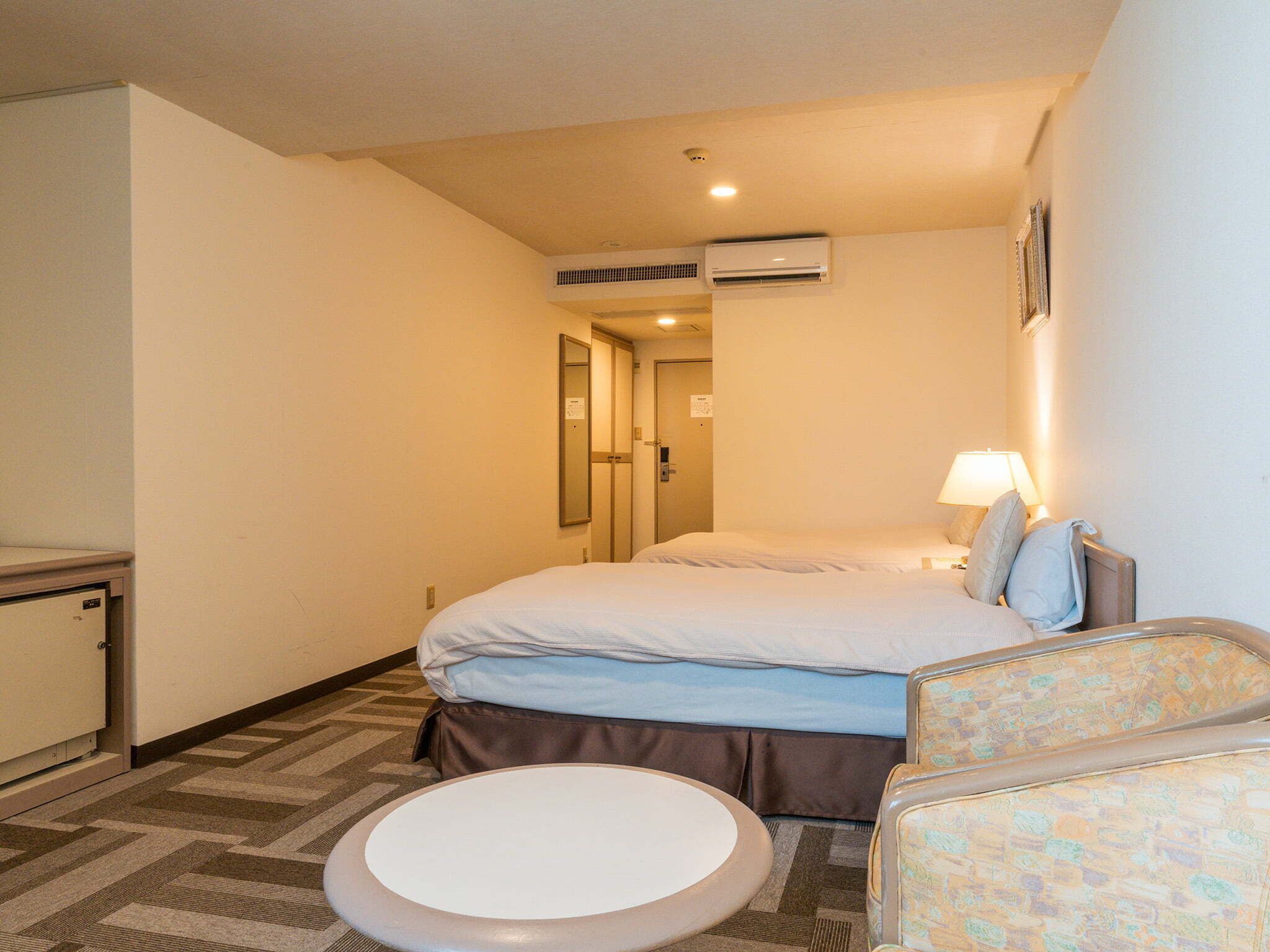 Una habitación de hotel con cama, una silla, una mesita y un equipo de aire acondicionado en la pared.
