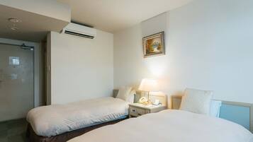 Habitación de hotel con dos camas, una mesita de noche con lámpara, un equipo de aire acondicionado y una puerta.