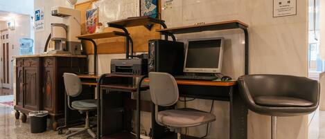 A workspace with a computer, chairs, and a coffee machine. There are signs on the wall indicating amenities and rules.
