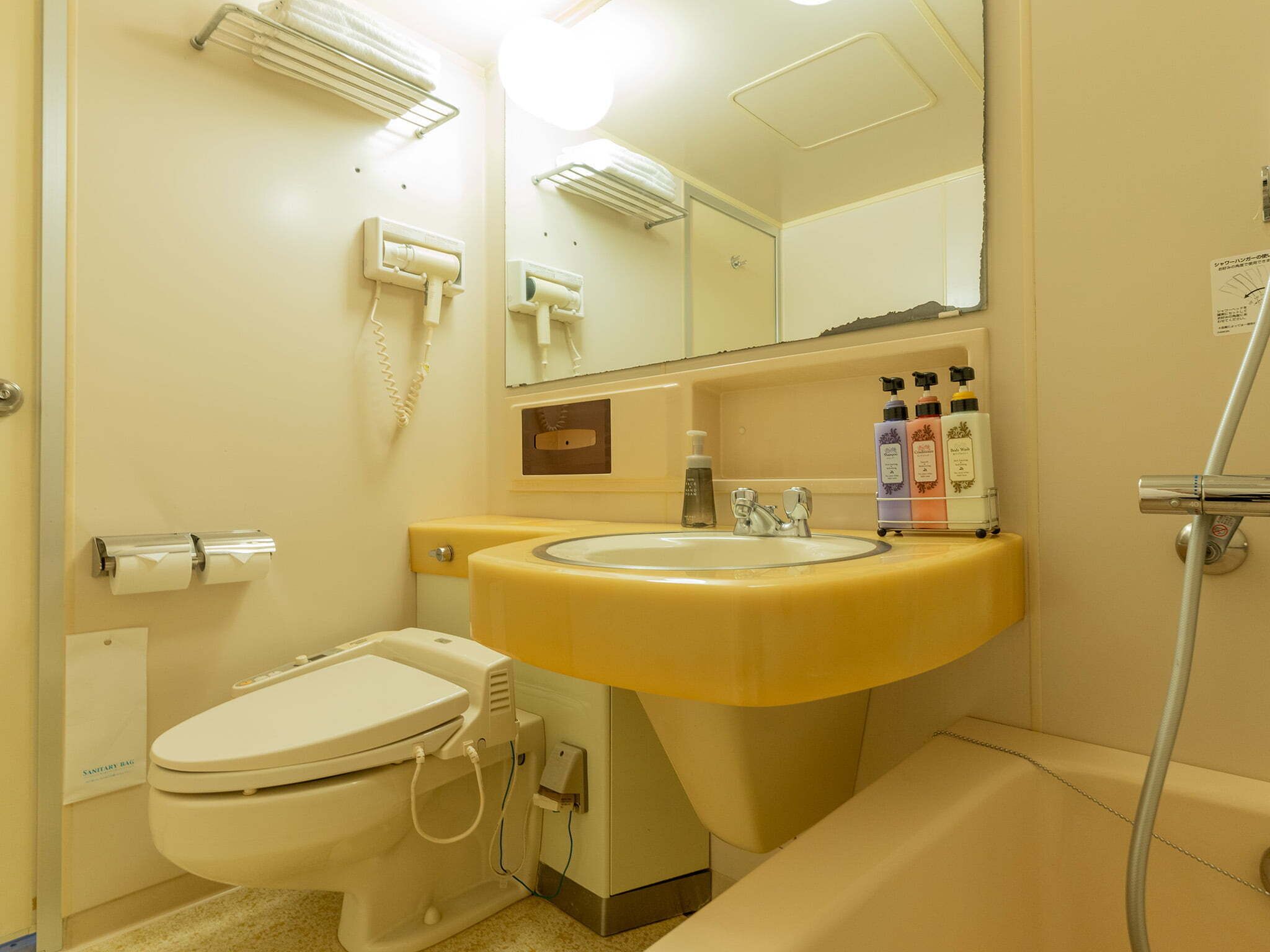 A bathroom with a toilet, sink, and mirror. There are toiletries on the sink counter.