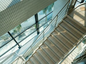 Un edificio moderno con fachada de vidrio, una escalera y vistas a palmeras.