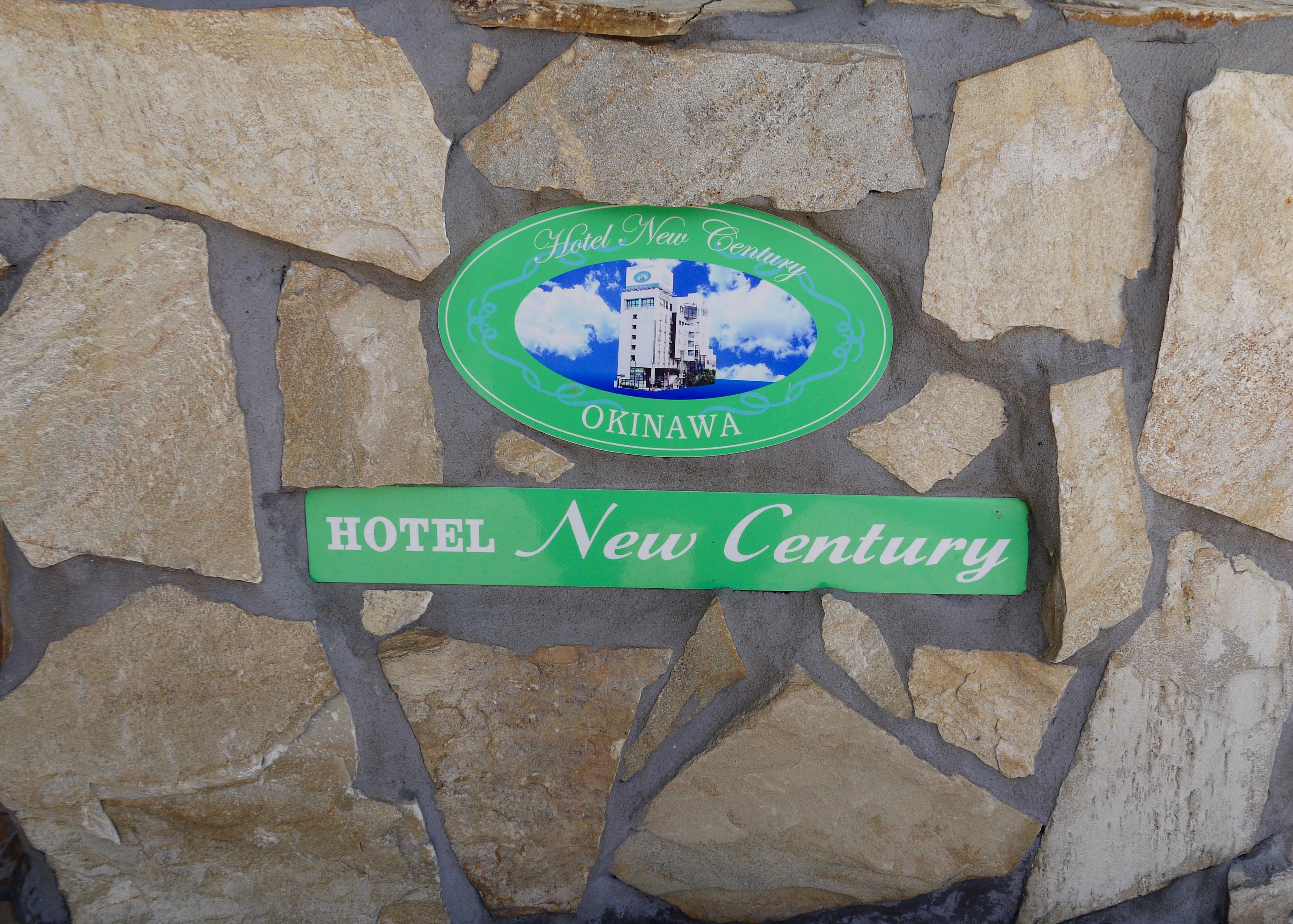 Señal del Hotel New Century en Okinawa, que muestra una ilustración del edificio y el nombre del hotel.